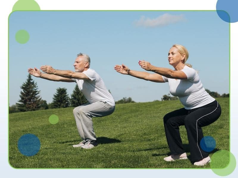 Two people in athletic wear performing squats on a grassy field under a clear blue sky, showcasing the importance of staying active over 60.